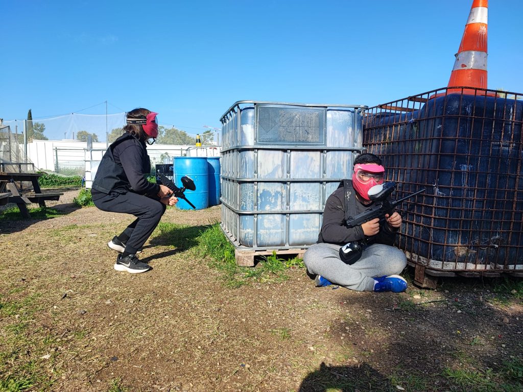 שני שחקנים בעמדת מחסה מאחורי מיכל במגרש הפיינטבול